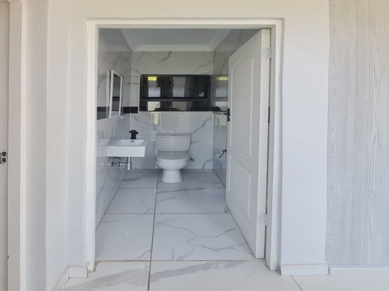 A modern, minimalist bathroom featuring marble-look wall and floor tiles, a wall-mounted basin, and a standard toilet.
