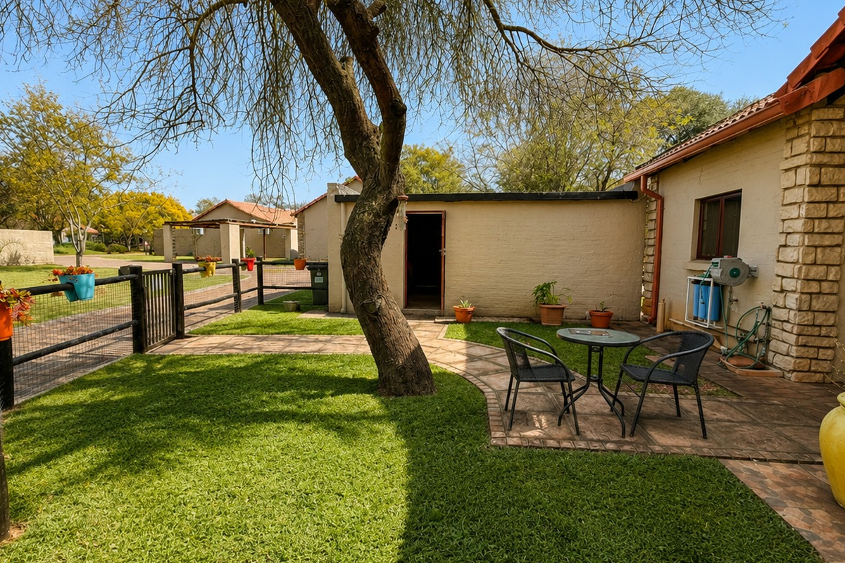 A well-maintained rear garden featuring a paved patio area, established lawn, and stone-clad exterior wall with an integrated water filtration system.