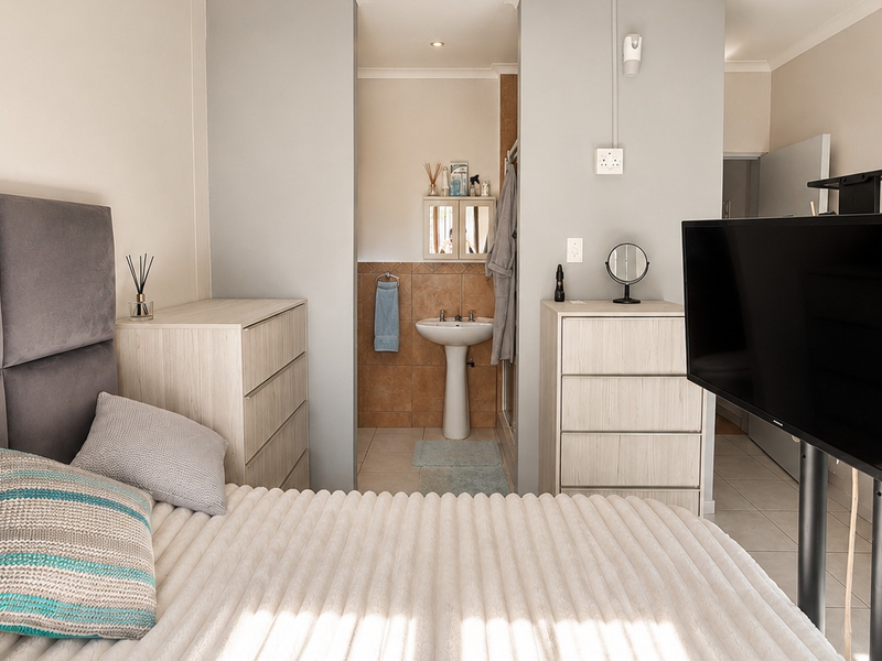 A bedroom featuring an open-plan layout with an integrated en-suite bathroom area, including a pedestal sink and shower enclosure.