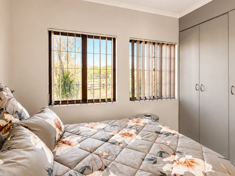 A well-maintained bedroom featuring built-in cupboards, vertical blinds, and security bars on the windows, offering a clean and functional living space.