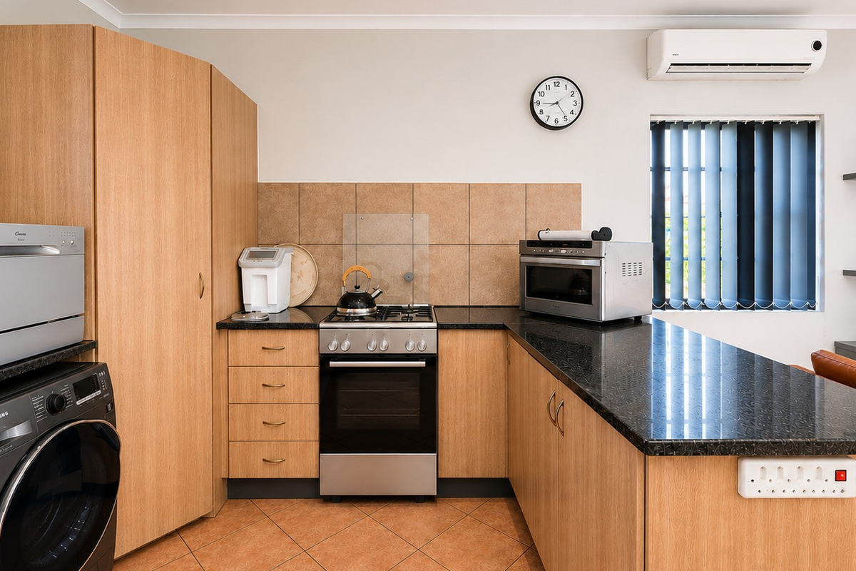 A functional kitchen featuring light wood cabinetry, dark granite countertops, a gas hob, electric oven, and tiled flooring with an integrated air conditioning unit.