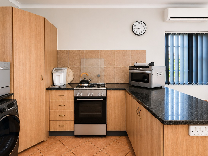 A functional kitchen featuring light wood cabinetry, dark granite countertops, a gas hob, electric oven, and tiled flooring with an integrated air conditioning unit.