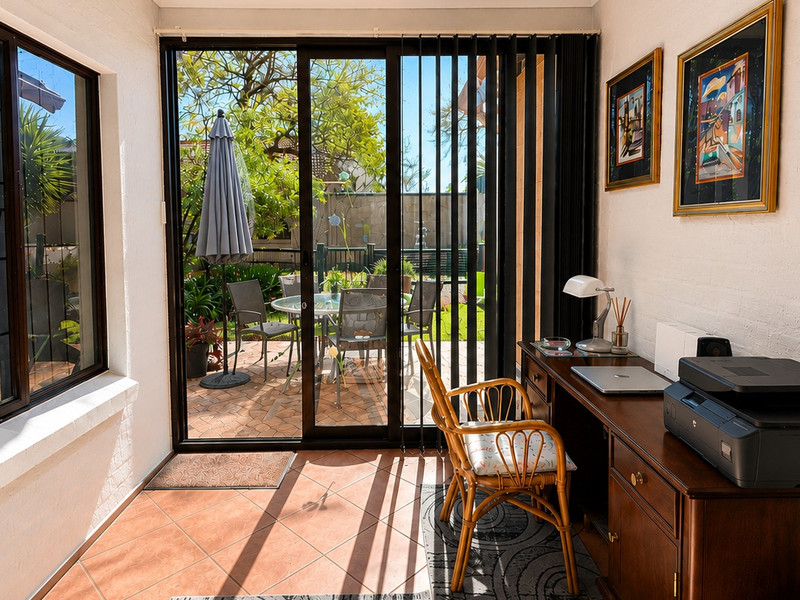 A bright sunroom or enclosed patio featuring tiled flooring and large sliding glass doors that provide direct access to the outdoor garden area.