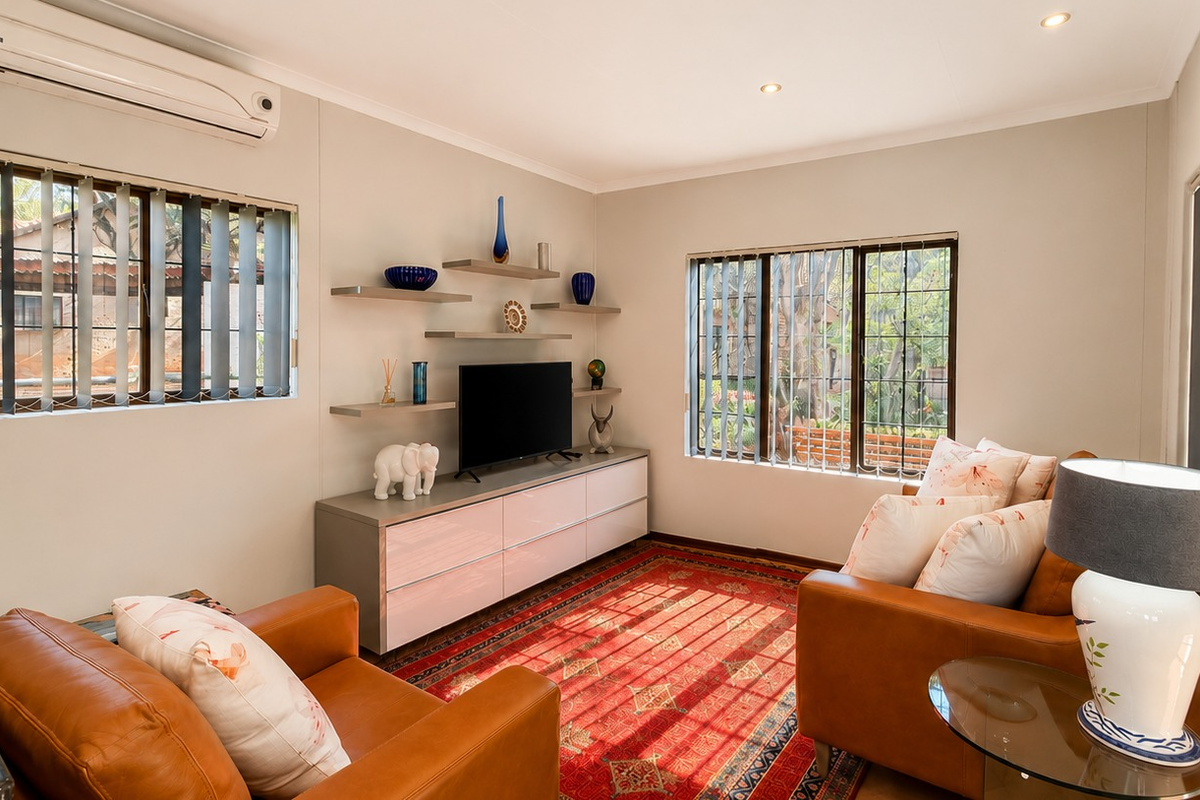 A well-maintained living room featuring split-system air conditioning, recessed downlighting, and built-in shelving units, with large windows providing natural light.