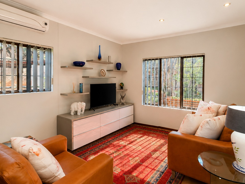 A well-maintained living room featuring split-system air conditioning, recessed downlighting, and built-in shelving units, with large windows providing natural light.