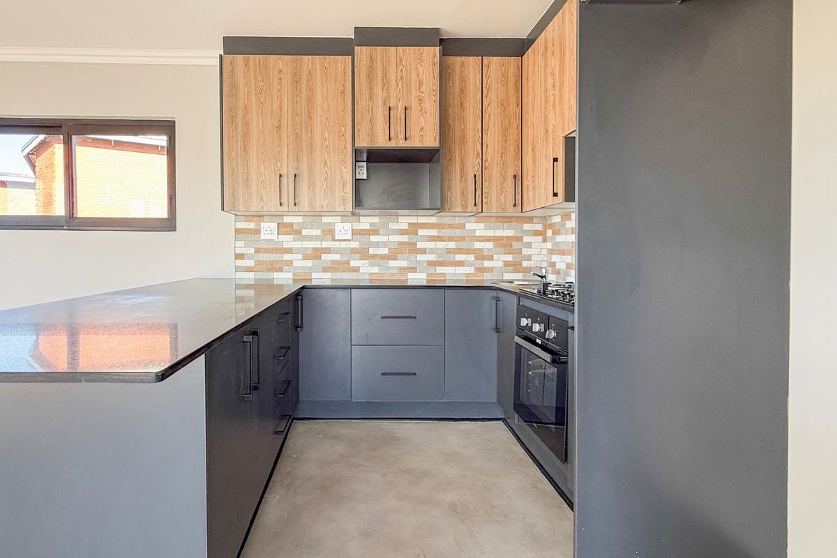 Modern kitchen featuring two-tone cabinetry, stone countertops, a built-in oven, gas hob, and a functional kitchen island with a tiled backsplash.