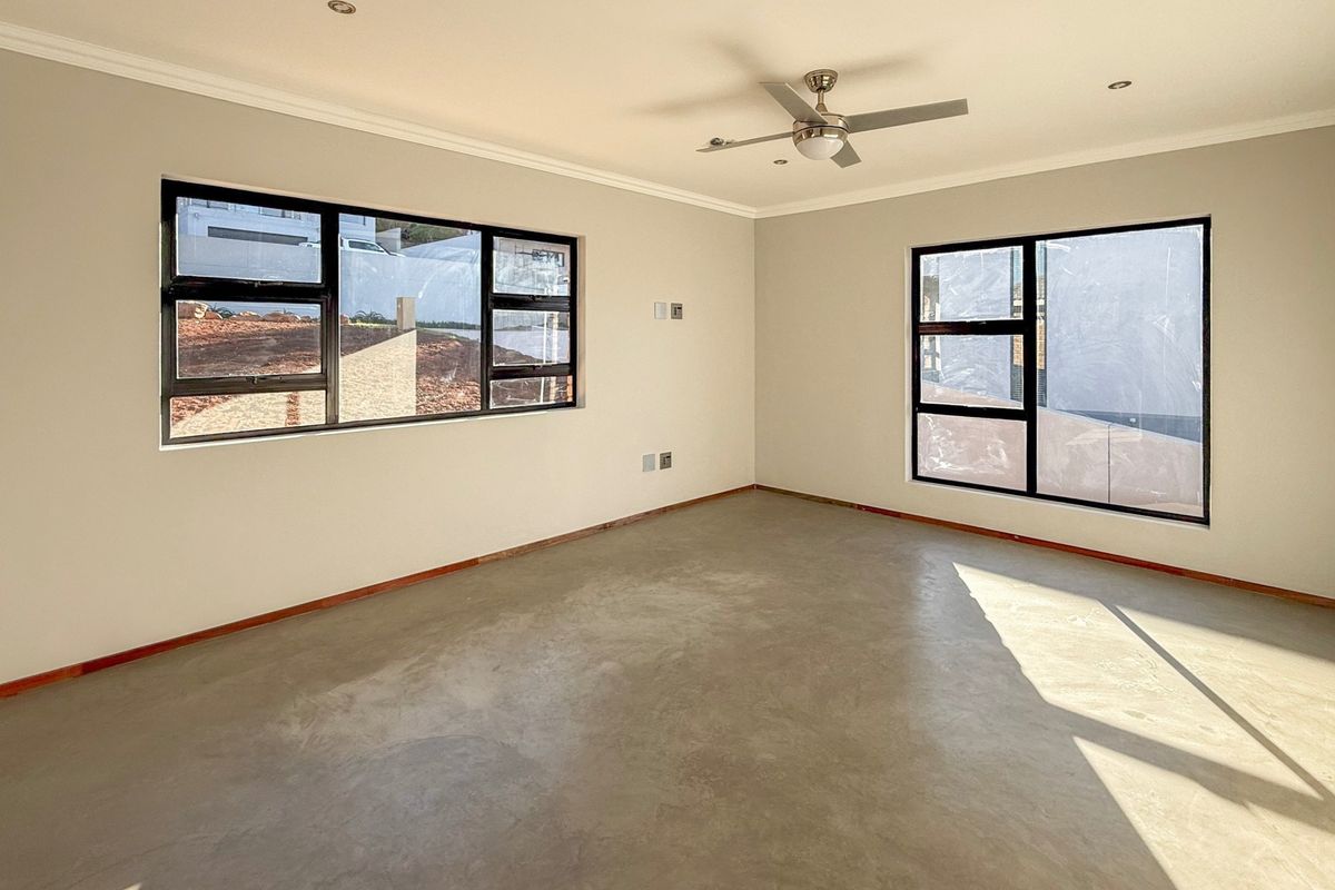 A bright, empty living room featuring polished concrete floors, modern aluminium-framed windows, a ceiling fan, and recessed lighting.