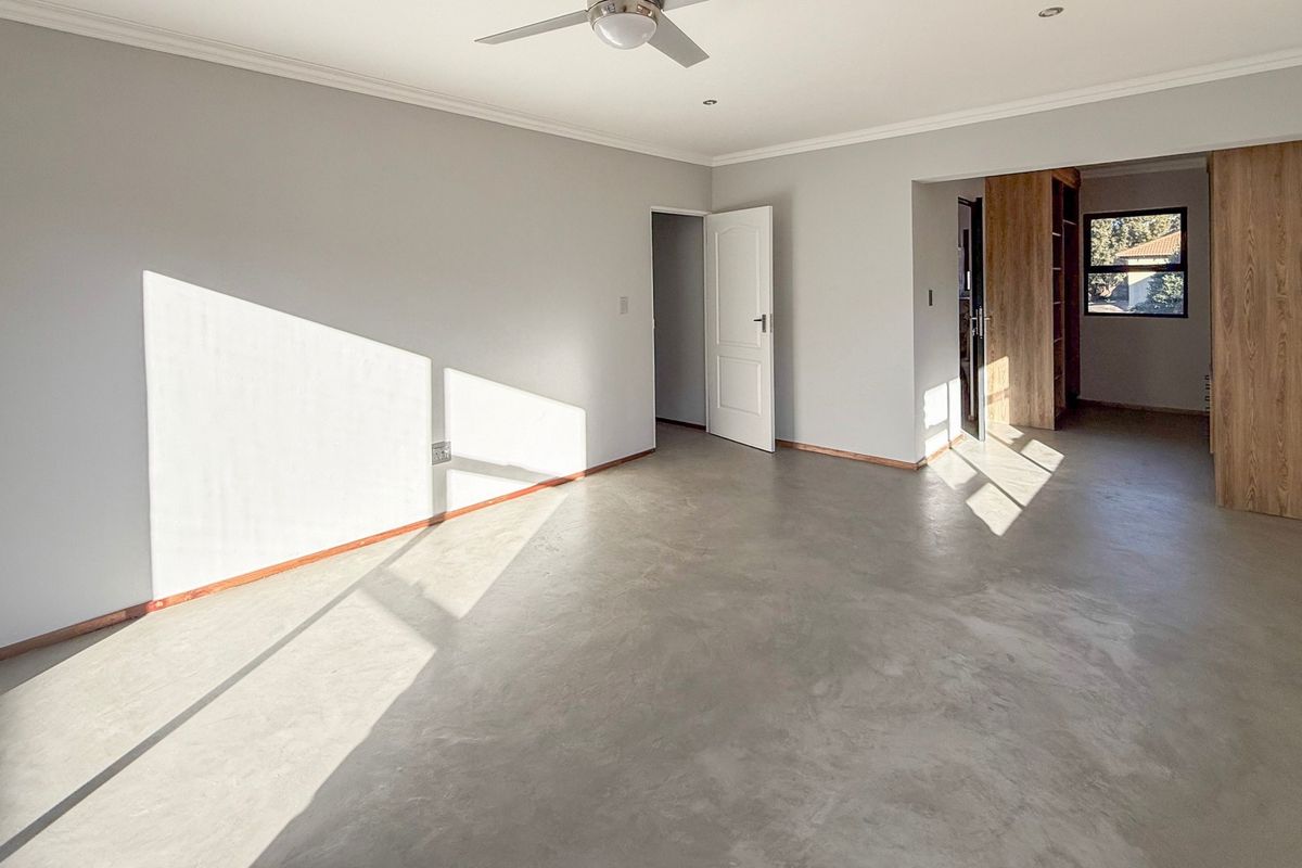 Spacious bedroom featuring polished concrete flooring, built-in cupboards, and a ceiling fan, offering a clean and modern blank canvas.
