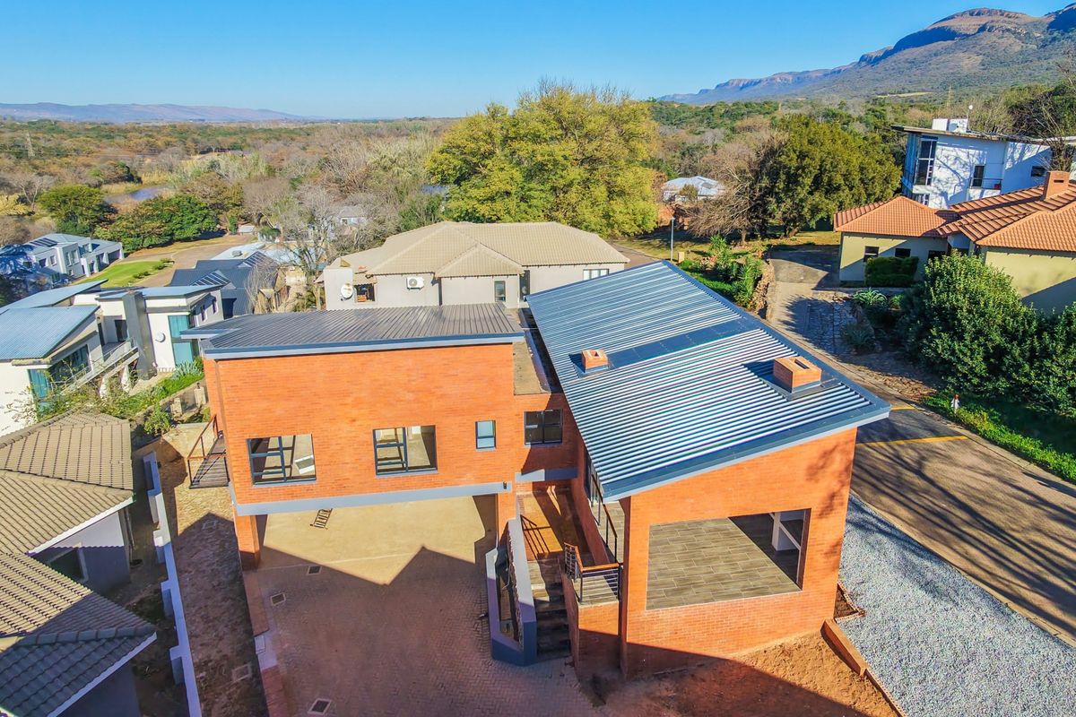 Aerial view of a modern double-story house featuring exposed brick walls, a corrugated metal roof, and a paved driveway in a residential estate.