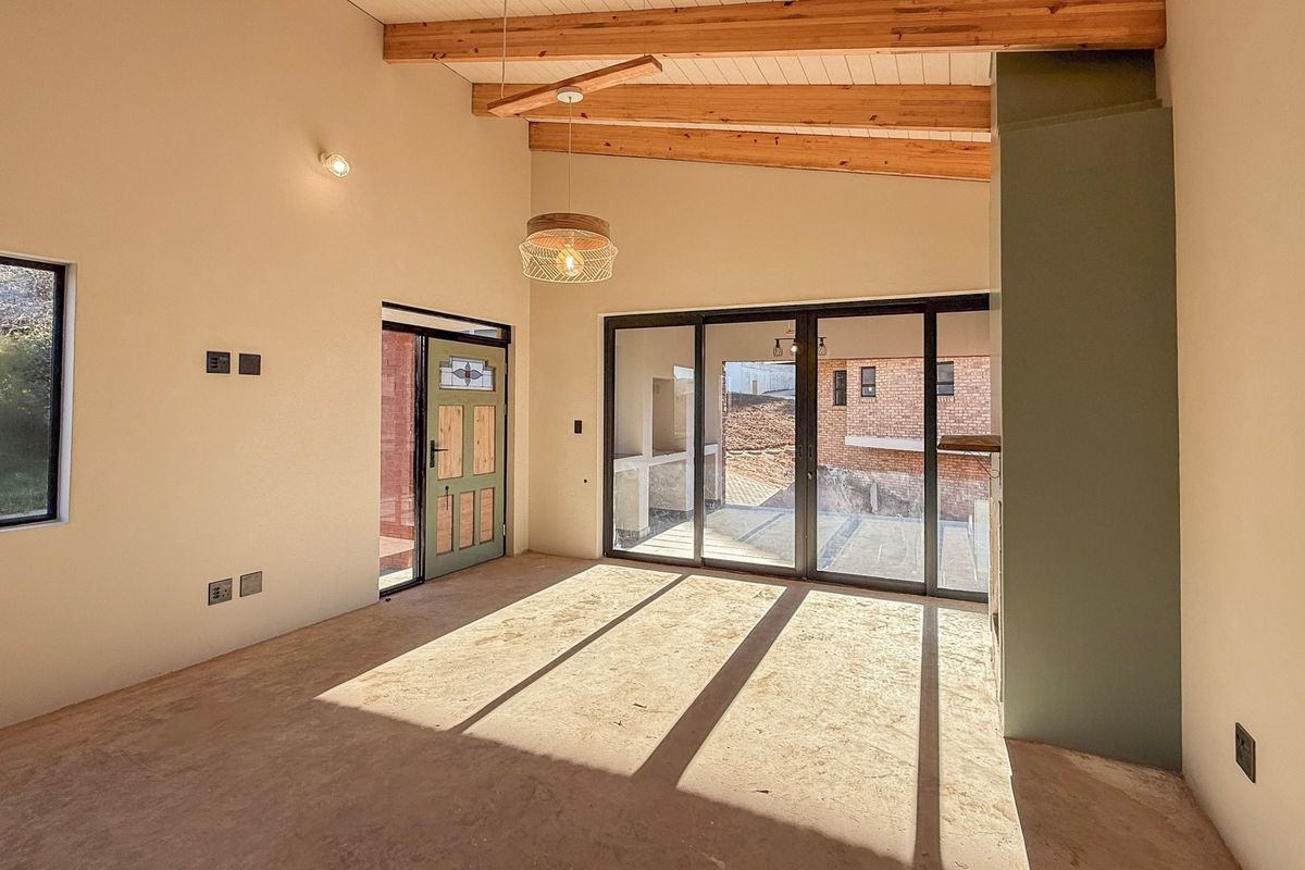 Spacious living area featuring exposed timber ceiling beams, large sliding glass doors providing natural light, and an unfinished floor ready for final finishes.