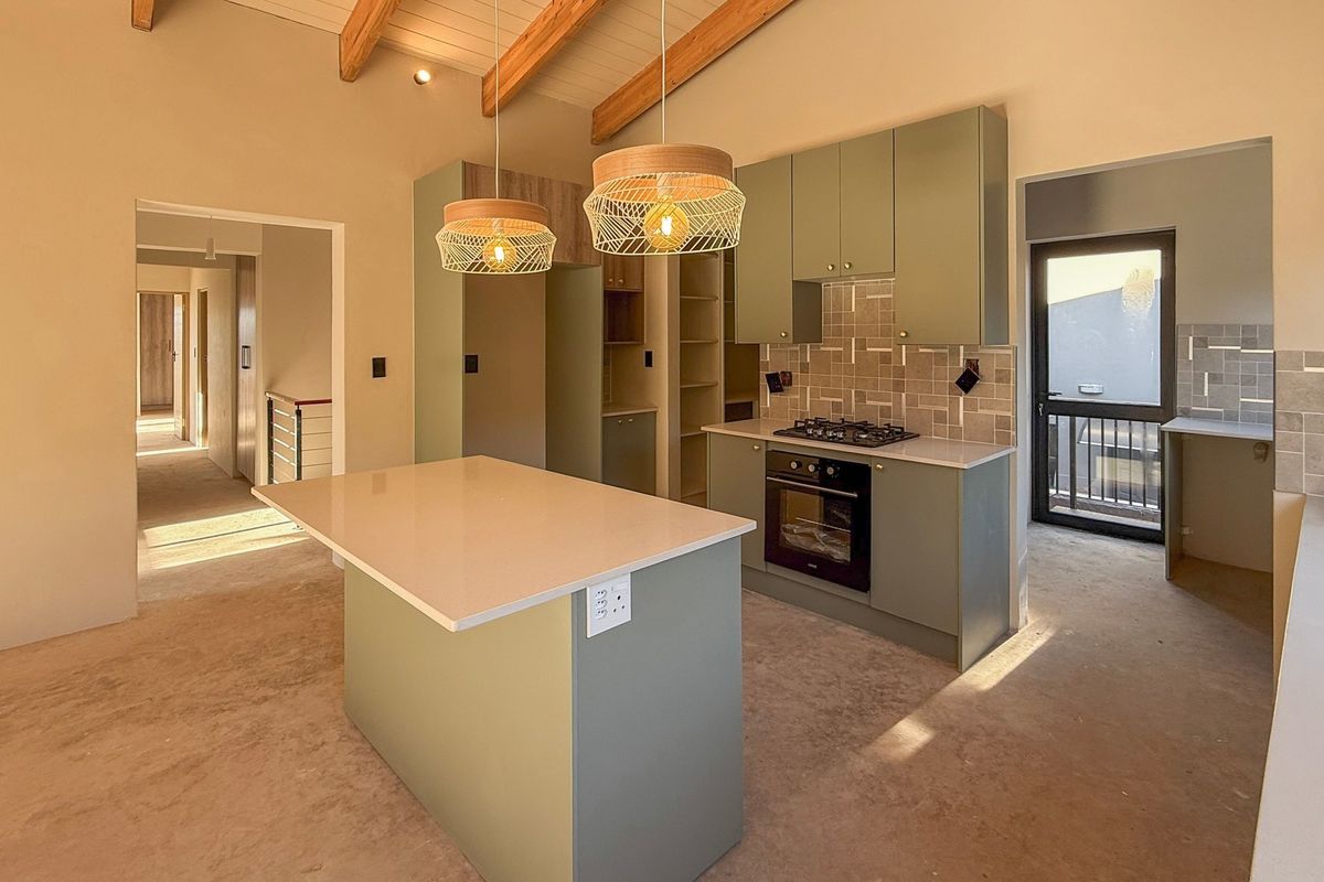 Modern kitchen featuring sage green cabinetry, a central island, built-in oven, gas hob, and exposed timber ceiling beams in an open-plan layout.