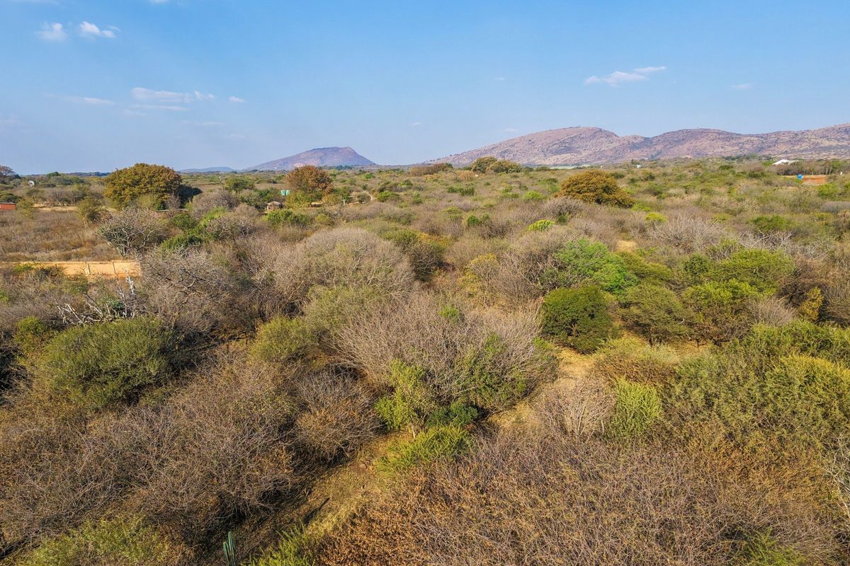 An aerial view of a large, undeveloped residential plot featuring native bushveld vegetation and scenic mountain views in the distance.