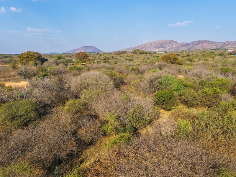 An aerial view of a large, undeveloped residential plot featuring native bushveld vegetation and scenic mountain views in the distance.