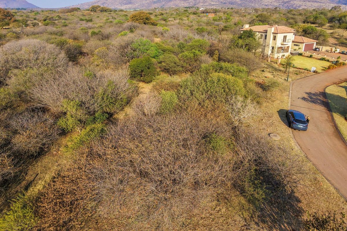 Aerial view of a vacant residential plot featuring native bushveld vegetation and adjacent paved road access in a scenic estate setting.