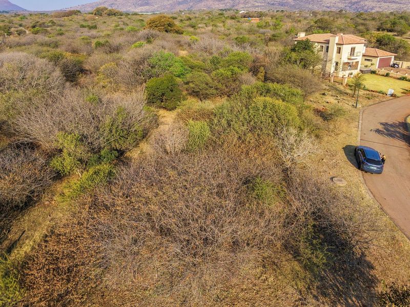 Aerial view of a vacant residential plot featuring native bushveld vegetation and adjacent paved road access in a scenic estate setting.