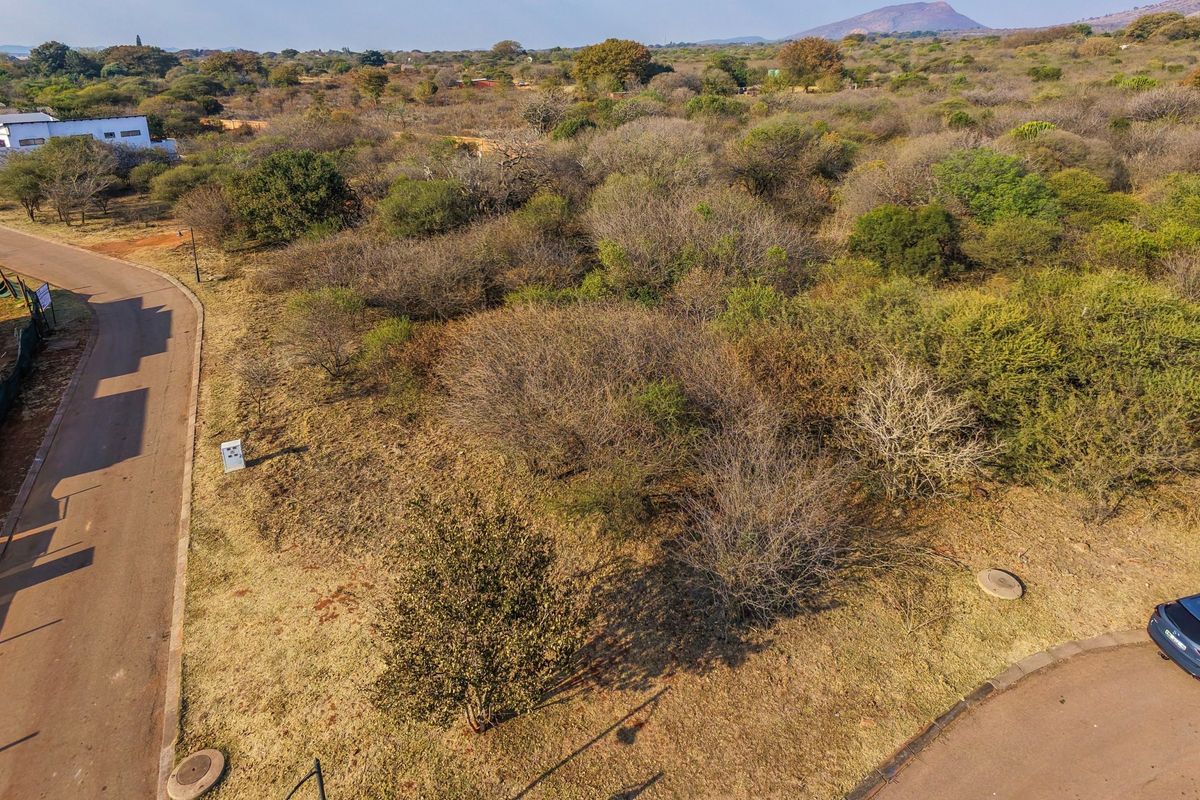 An aerial view of a vacant residential plot featuring natural vegetation, adjacent paved roads, and established utility access points in a suburban estate setting.