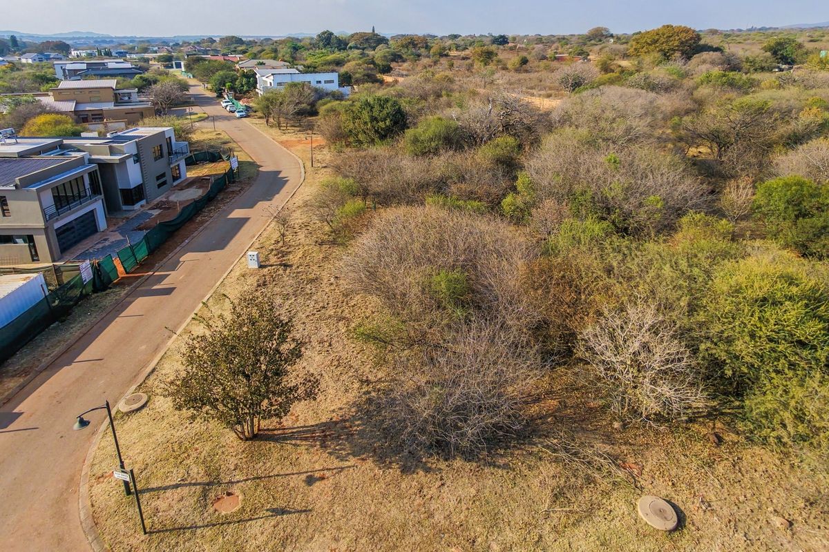 Aerial view of a vacant residential plot featuring natural vegetation, adjacent to a paved street with existing utility infrastructure.