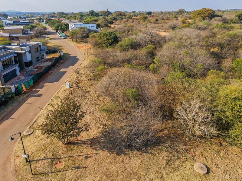 Aerial view of a vacant residential plot featuring natural vegetation, adjacent to a paved street with existing utility infrastructure.