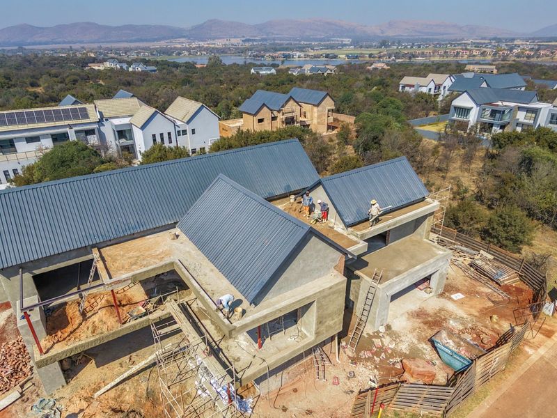 Aerial view of a residential property under construction, featuring a completed metal roof and ongoing structural work on the exterior walls.