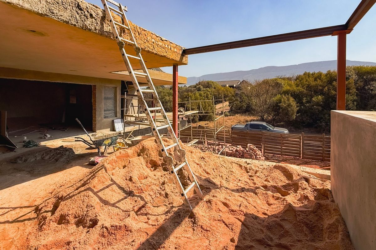 Rear exterior view of a property currently undergoing significant construction and renovation, featuring exposed structural steel and unfinished concrete surfaces.
