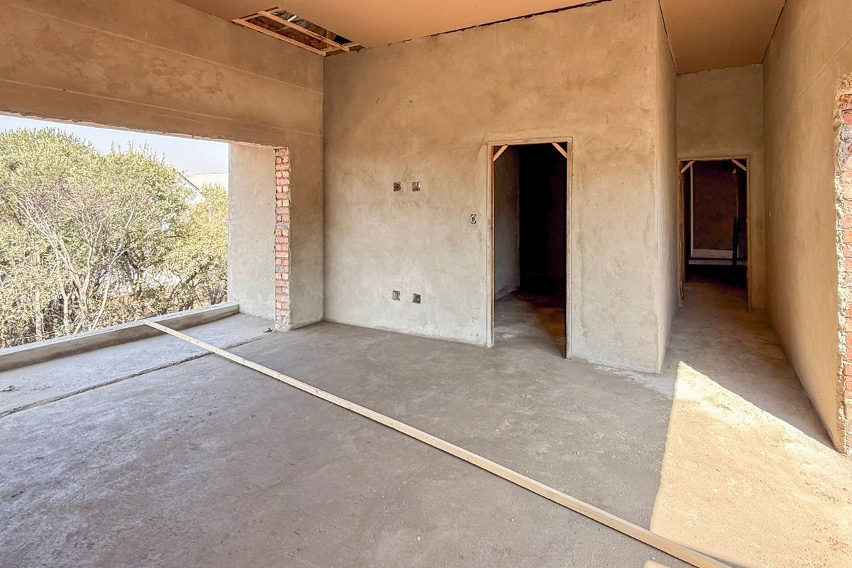 An unfinished living room space in a construction phase, featuring raw plastered walls, exposed brickwork, and concrete flooring, awaiting final finishes and interior design.