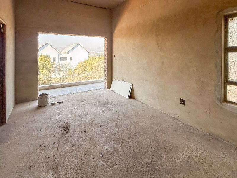 An unfinished bedroom interior featuring raw plastered walls, concrete flooring, and a large opening leading to an outdoor balcony area.