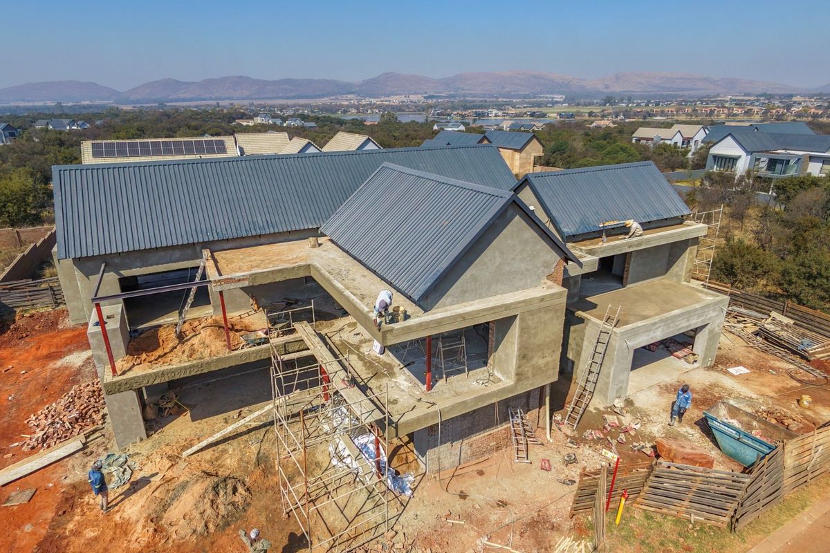 Aerial view of a residential property under construction, featuring a completed metal roof with solar panels and an unfinished concrete structure.