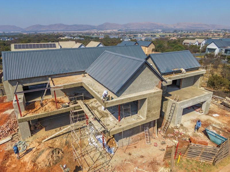 Aerial view of a residential property under construction, featuring a completed metal roof with solar panels and an unfinished concrete structure.