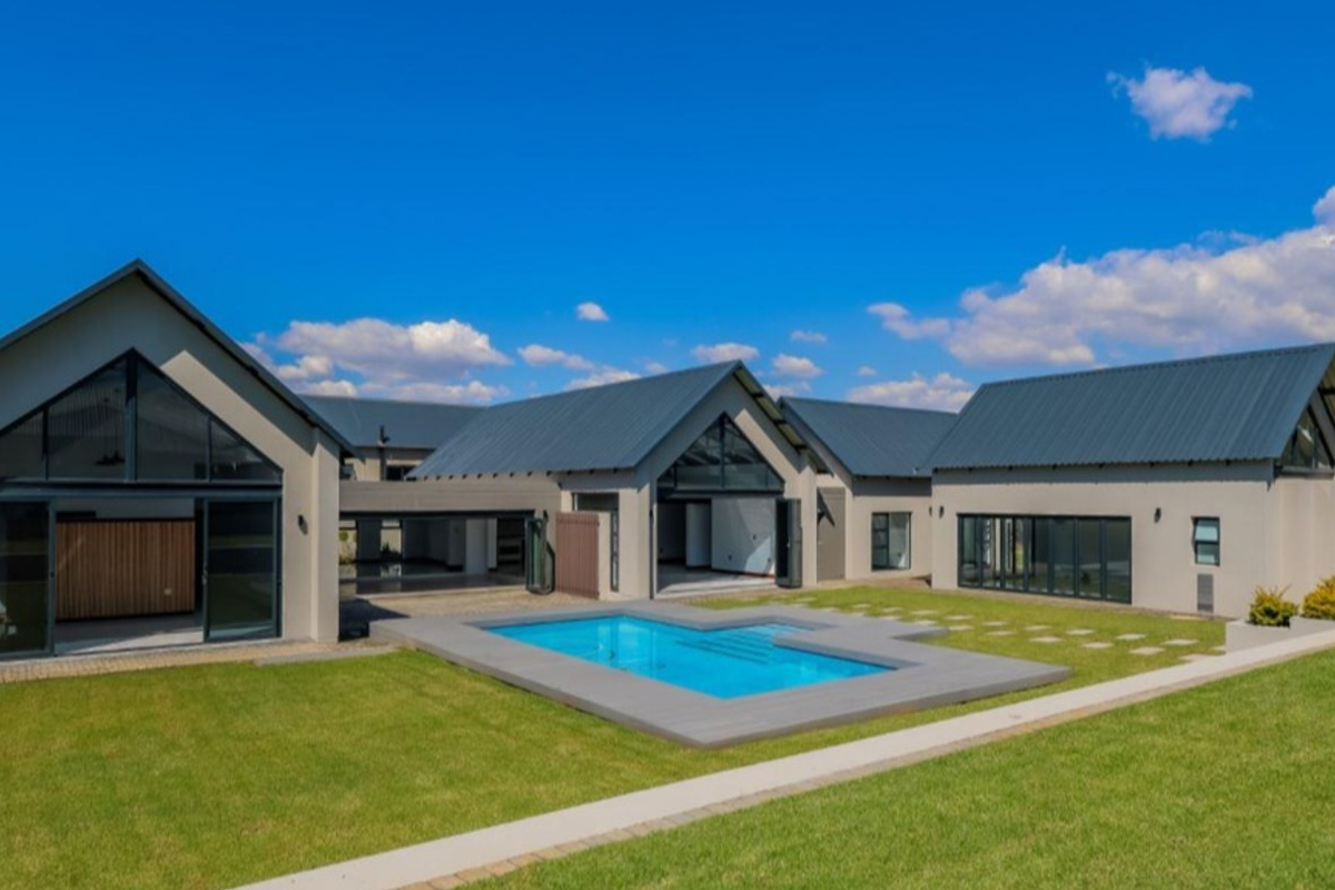 Modern rear elevation featuring a swimming pool, expansive lawn, and large glass sliding doors connecting the interior living spaces to the outdoor area.