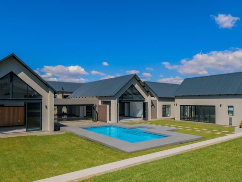 Modern rear elevation featuring a swimming pool, expansive lawn, and large glass sliding doors connecting the interior living spaces to the outdoor area.