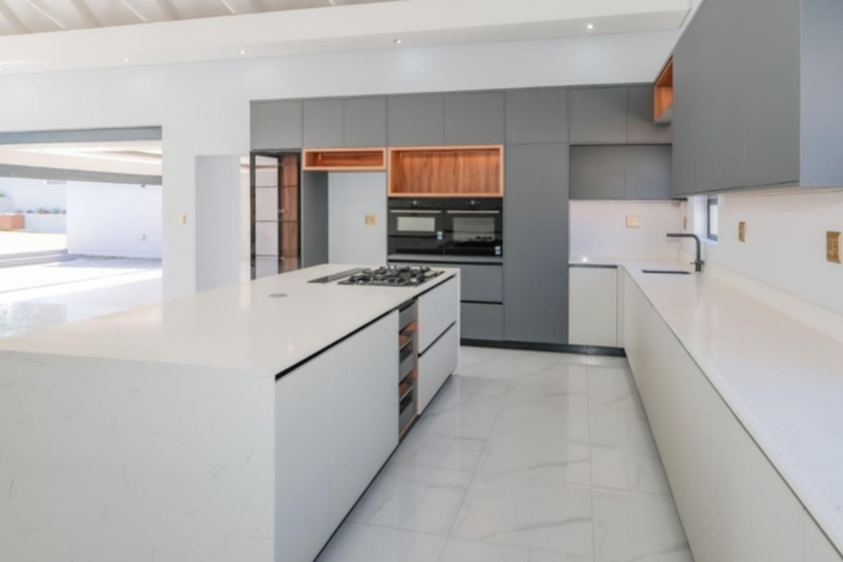 Modern, spacious kitchen featuring a large central island with quartz countertops, integrated cabinetry, built-in oven, gas cooktop, and sleek tiled flooring.
