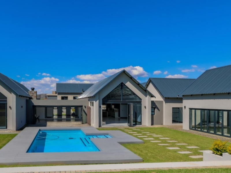 A modern rear exterior view featuring a swimming pool with decking, expansive bi-fold doors, and contemporary architectural design with metal roofing.