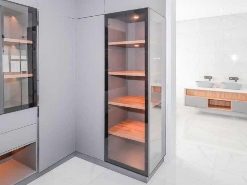 Modern bathroom featuring a sleek double vanity with wall-mounted faucets, high-gloss floor tiles, and integrated glass-fronted cabinetry for storage.