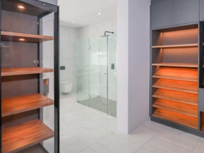 A modern, high-end bathroom featuring custom built-in cabinetry with integrated lighting, a frameless glass shower enclosure, and a wall-mounted toilet.