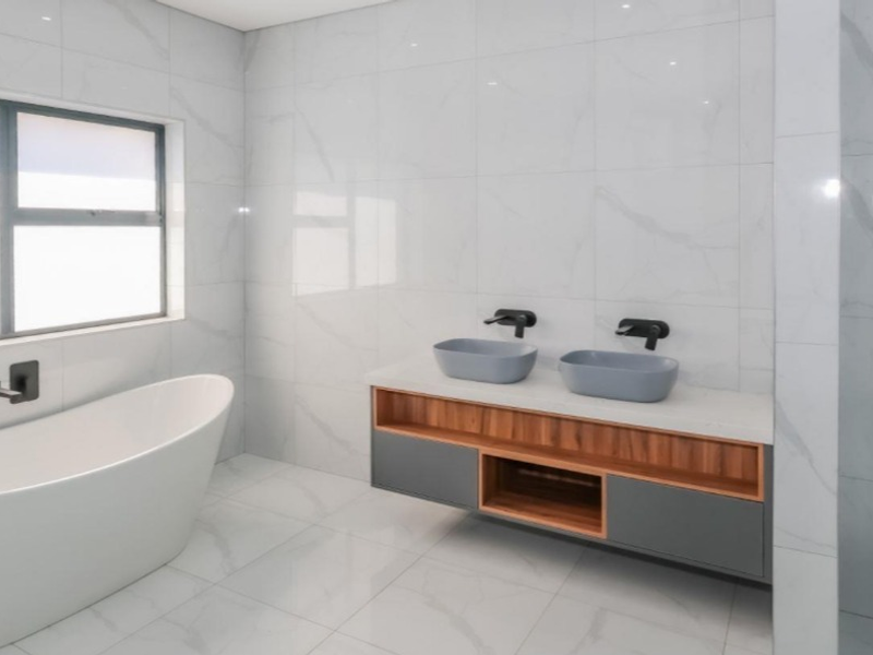 Modern bathroom featuring a sleek freestanding bathtub, double vanity with wall-mounted taps, and high-end marble-look tiling throughout.