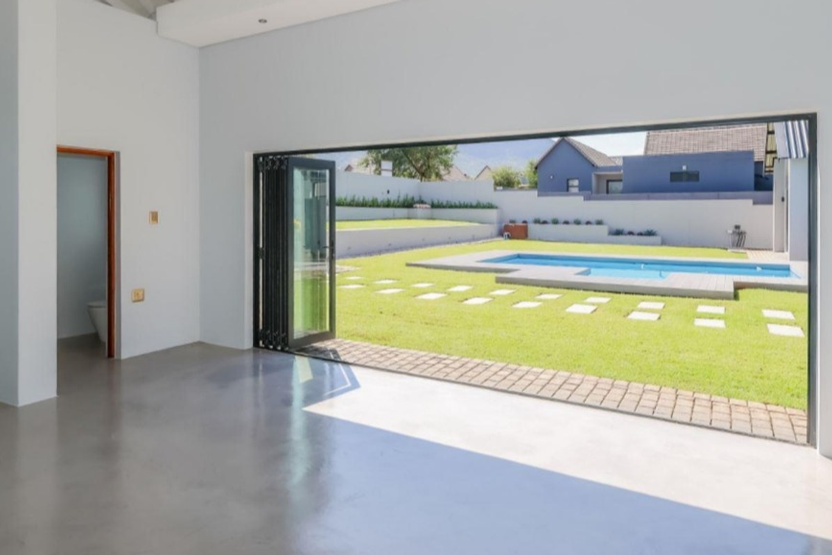 Spacious open-plan living area featuring polished concrete floors and large bi-fold doors opening onto a landscaped garden with a swimming pool.