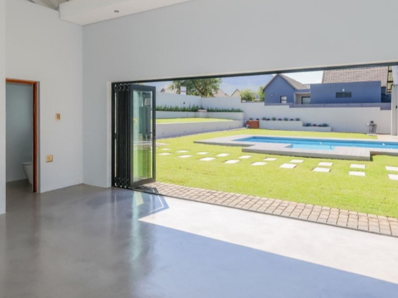 Spacious open-plan living area featuring polished concrete floors and large bi-fold doors opening onto a landscaped garden with a swimming pool.