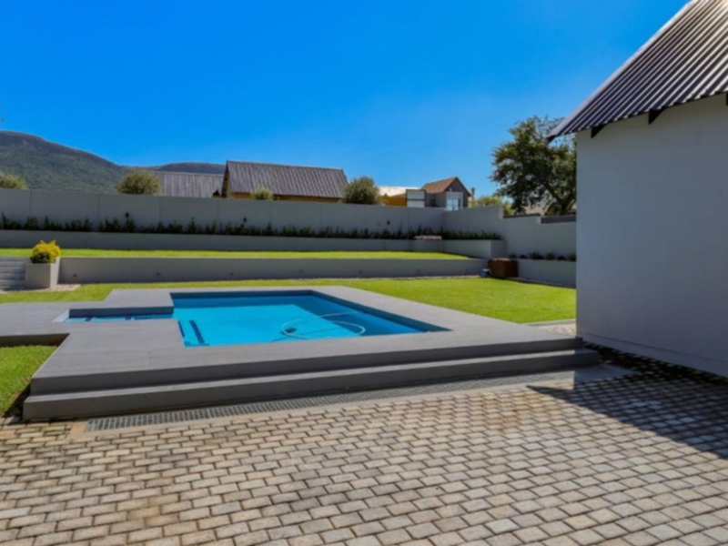 A well-maintained outdoor area featuring a swimming pool with timber decking, paved patio space, and tiered landscaped gardens against a mountain backdrop.