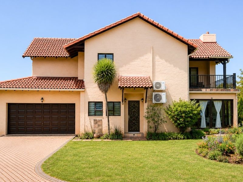 A well-maintained two-story townhouse featuring a terracotta tiled roof, paved driveway, double garage, and a private balcony overlooking a landscaped garden.