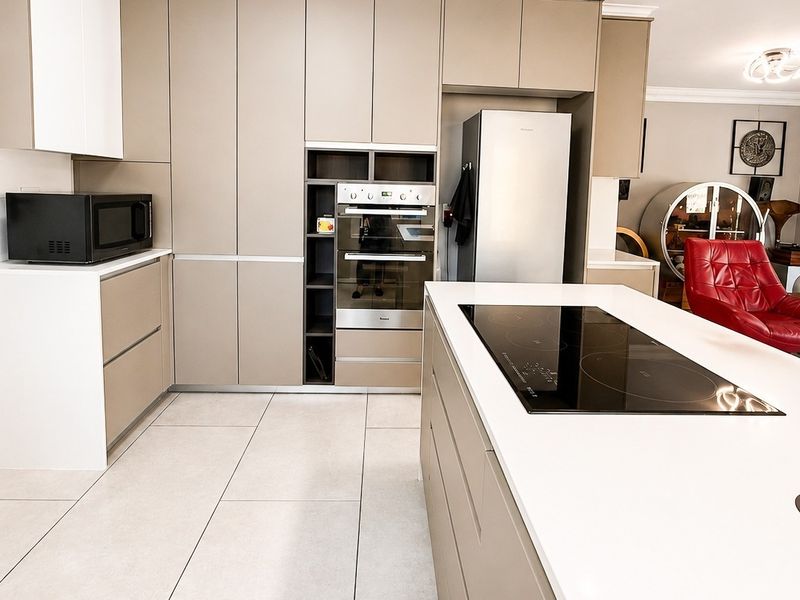 Modern open-plan kitchen featuring sleek cabinetry, a central island with an integrated electric cooktop, and high-quality tile flooring.