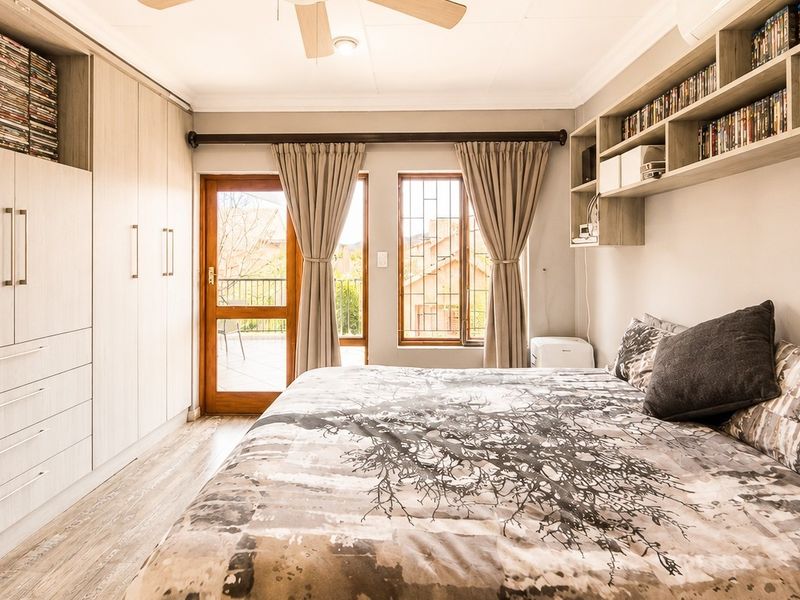 A well-maintained bedroom featuring extensive built-in cabinetry, floating shelving, laminate flooring, and direct access to a private balcony.