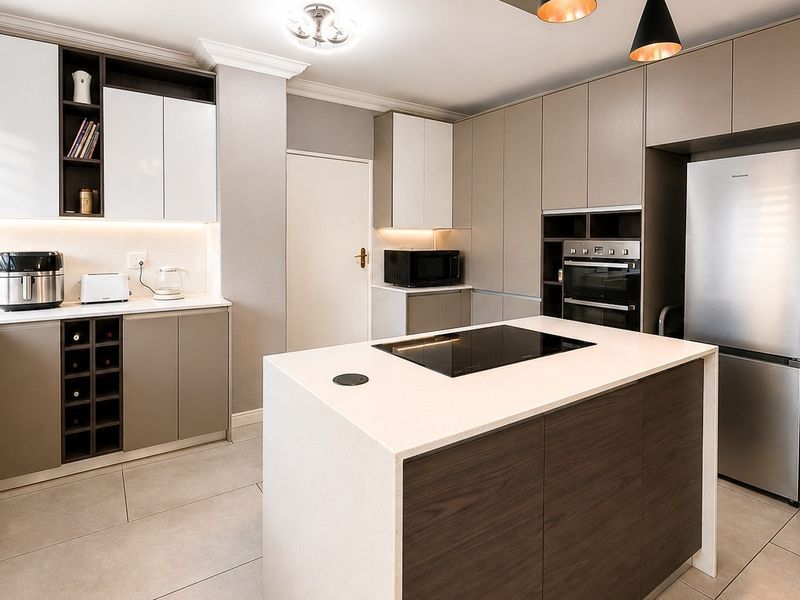 Modern kitchen featuring a central island with induction hob, sleek cabinetry, quartz countertops, built-in oven, and integrated under-cabinet lighting.