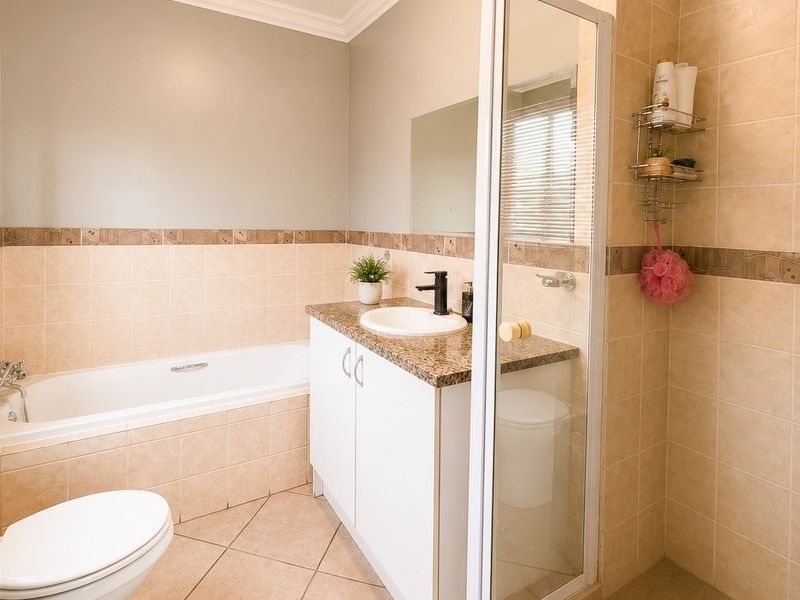 A well-maintained bathroom featuring a built-in vanity, drop-in basin, bathtub, and a separate shower enclosure with neutral wall and floor tiling.