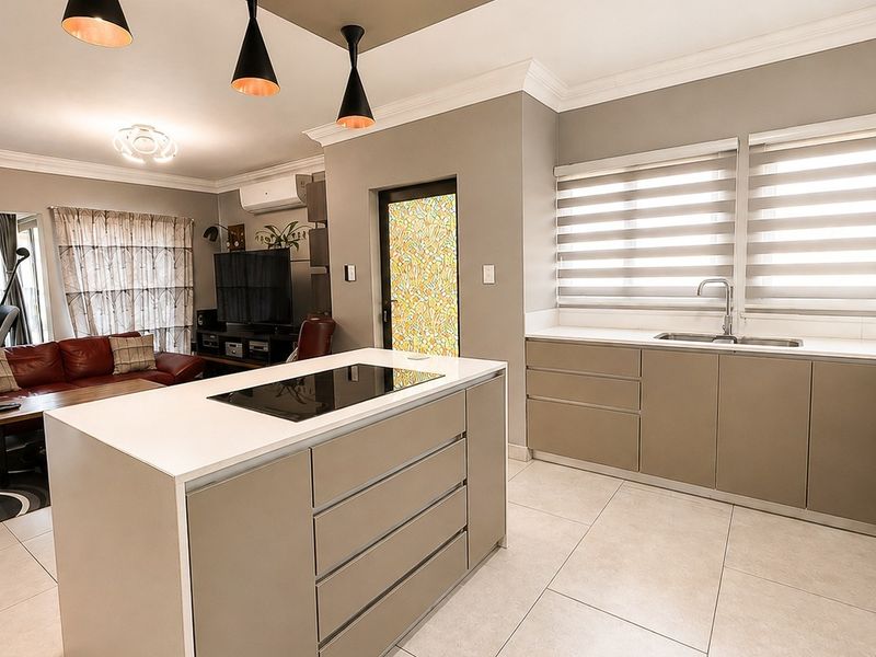 Modern open-plan living area featuring a sleek kitchen with a central island, built-in hob, stone countertops, and neutral tiled flooring throughout.