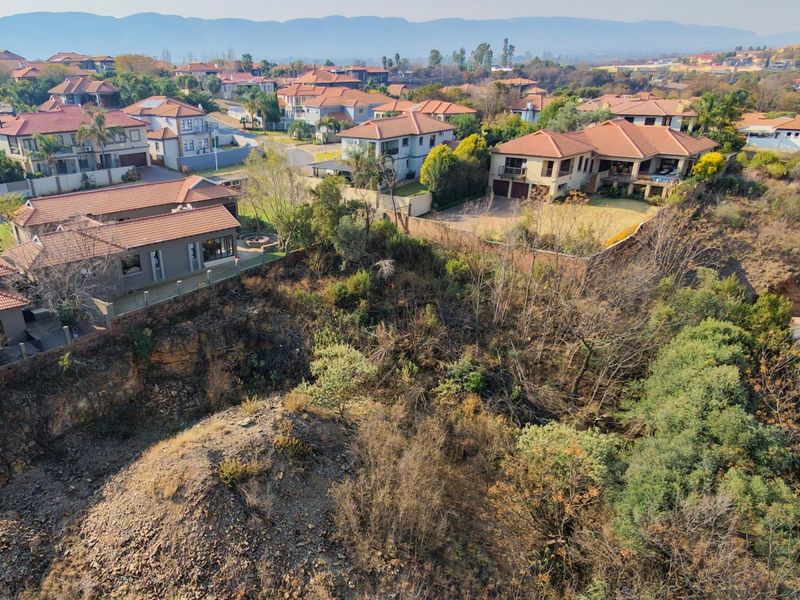 An aerial view of a vacant residential plot featuring natural vegetation and rocky terrain, situated within an established suburban estate.