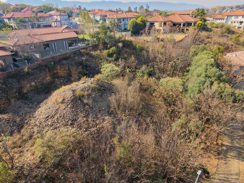 Aerial view of a vacant residential plot featuring sloped terrain, rocky outcrops, and established vegetation within a developed estate.