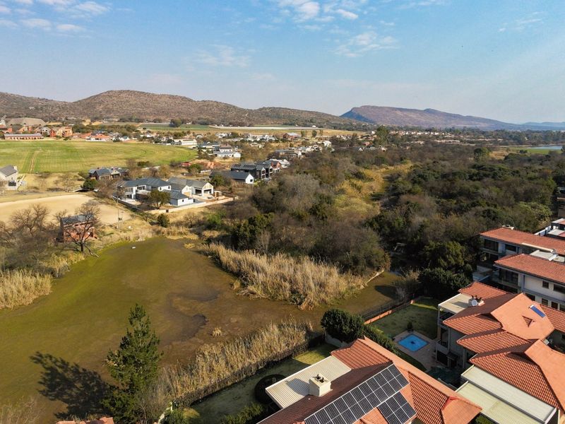 Aerial view of a residential estate featuring tiled roof homes, solar installations, and surrounding natural landscape with wetland areas and distant mountains.
