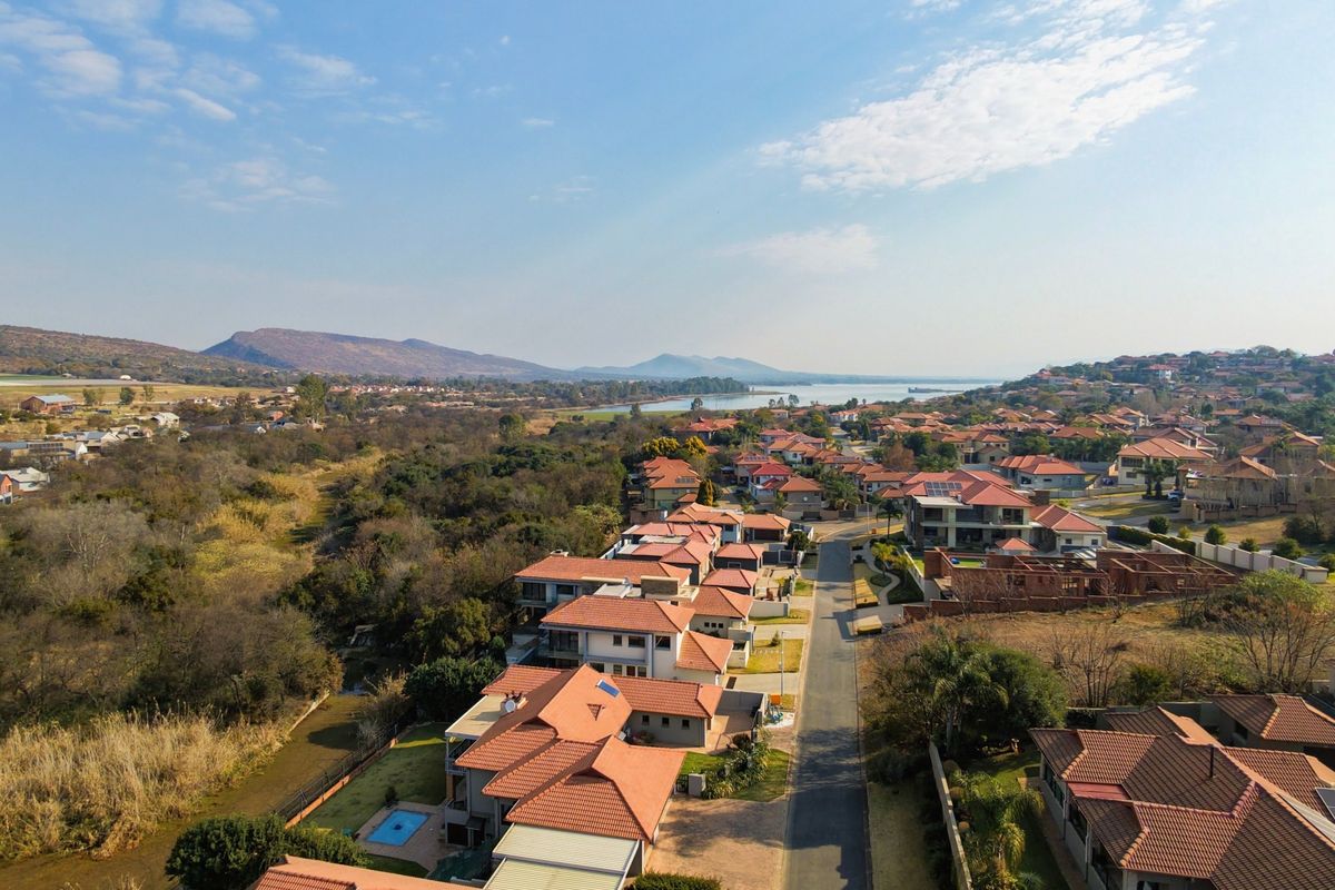 An aerial view of a residential estate featuring multiple homes with tiled roofs, swimming pools, and surrounding natural landscape.