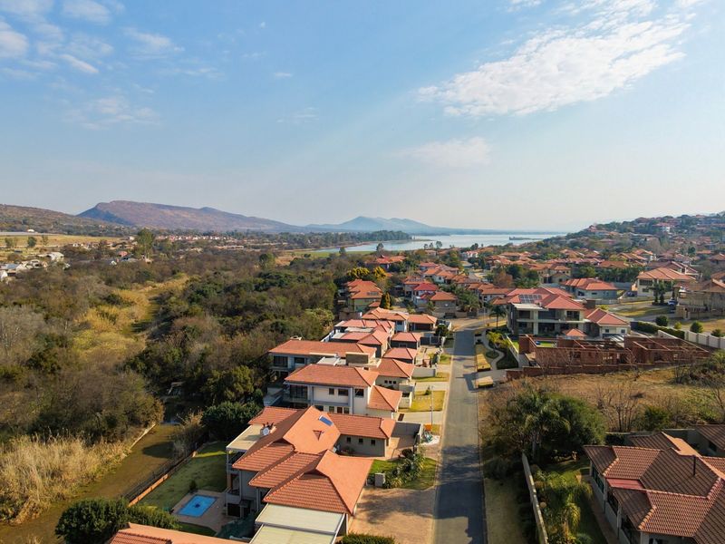 An aerial view of a residential estate featuring multiple homes with tiled roofs, swimming pools, and surrounding natural landscape.