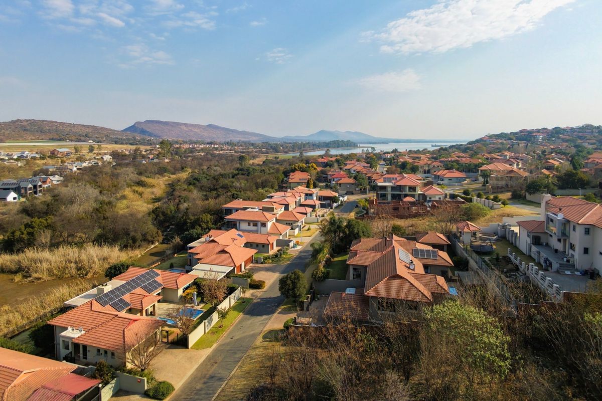 An aerial view of a residential estate featuring multiple homes with tiled roofs, solar panels, and surrounding natural landscape.